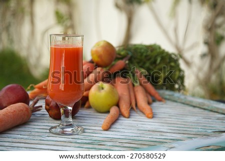 A glass of fresh apple carrot juice on a wooden surface. Fresh carrots and apples in the background.Copy space