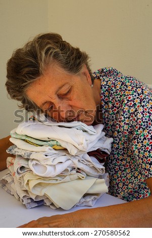 A senior woman between 70 and 80 fell in asleep from tiredness on a pile of ironed cloths
