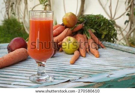 A glass of fresh apple carrot juice on a wooden surface. Fresh carrots and apples in the background.Copy space.Close up