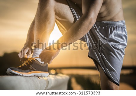 Man tying jogging shoes.A person running outdoors on a sunny day. The person is wearing black running shoes.Focus on a side view of two human hands reaching down to a athletic shoe.
