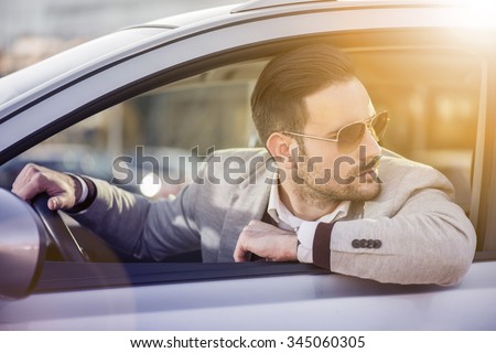 Close up of a handsome man siting in his car.He is wearing a white shirt and a grey suit.