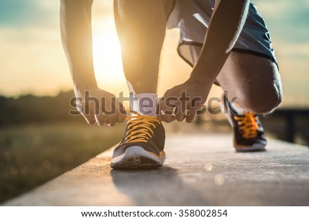 Man tying jogging shoes.A person running outdoors on a sunny day.Focus on a side view of two human hands reaching down to a athletic shoe.