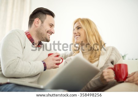 Couple sitting on sofa with laptop and a cup of coffee.They are sitting close to each other and drinking coffee.