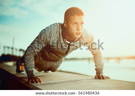Picture of a young athletic man doing push ups outdoors.Fitness and exercising outdoors urban environment.Selective focus