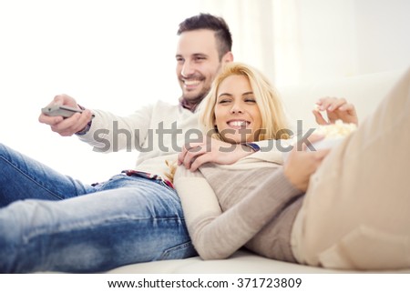 Happy young couple lying on the sofa at home with popcorn watching TV