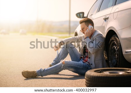 A young man with a silver car that broke down on the road.He is waiting for the technician to arrive.