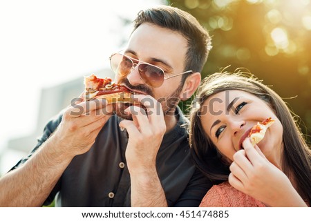 Happy attractive young couple romantically eating a fresh pizza outdoors.