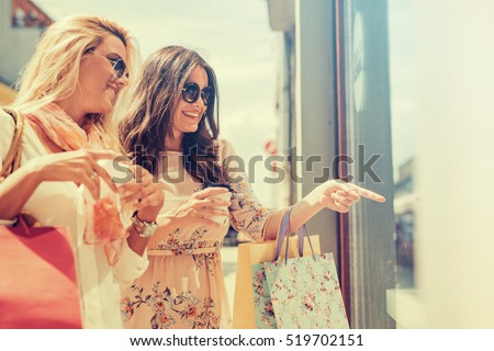 Happy woman with shopping bags pointing finger in the shop window.
