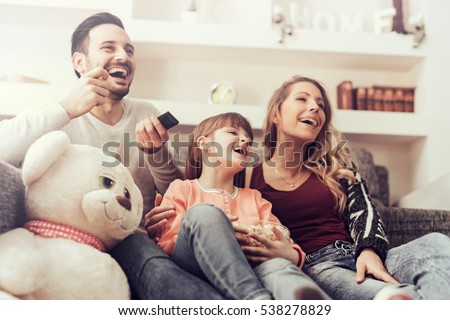 Young family watching TV together at home and having fun together.