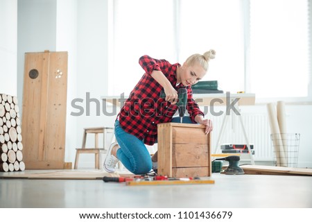 Indoor shot of young woman repairing furniture at home, sitting on the floor.