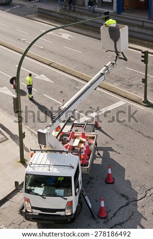 utility service company electrician worker repairs traffic lights from elevator bucket truck in the city