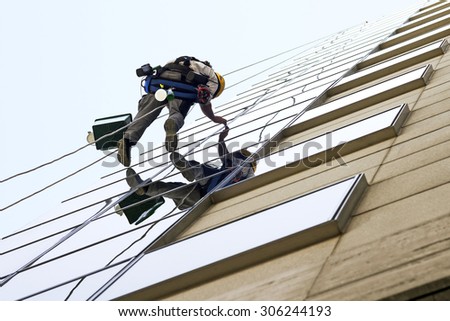 vertical climber worker hanging on ropes to cleaning the windows of a modern building