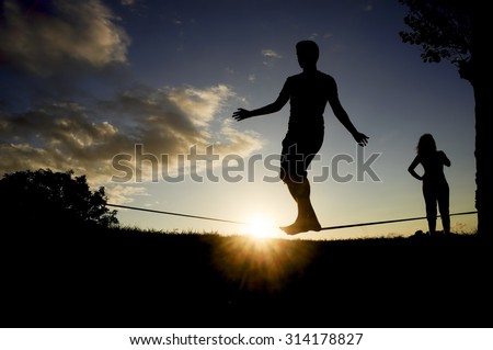 couple man and  woman  balancing in slack line , slacklining , sport in nature at sunset
