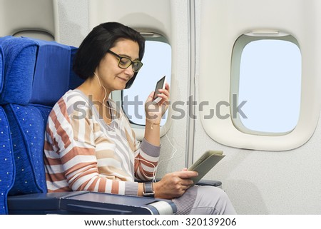 caucasian woman passenger in airplane using mobile and  tablet smart devices with headphones