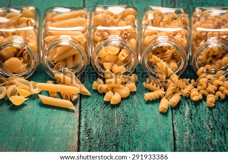 Various mix of pasta on wooden rustic background, sack ,bowl,jar,and wooden spoons. Diet and food concept.