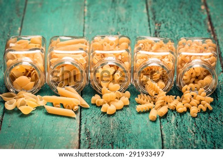 Various mix of pasta on wooden rustic background, sack ,bowl,jar,and wooden spoons. Diet and food concept.