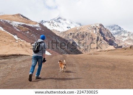 Traveler man and dog running on the road of  Kazbegi-Gergeti village, Georgia, Caucasus
