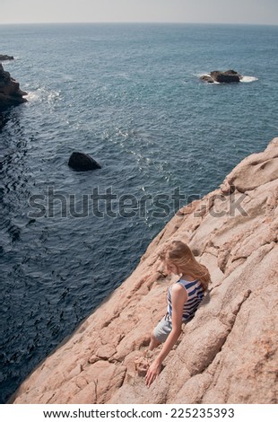 Young woman looking down into the ocean on the rocks