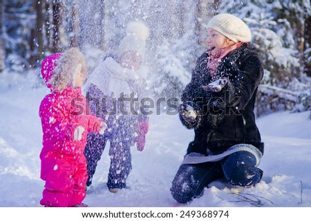 Mother and two children playing with snow in winter forest