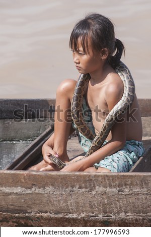 TONLE SAP, CAMBODIA - JAN 1, 2013: Unidentified little asian girl holding snake on her shoulders in Ton le Sap water village, near Siam Reap,Cambodia on January 1, 2013.