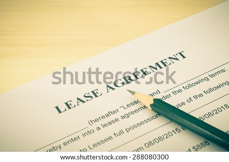 Lease agreement contract sheet and brown pencil at bottom right corner on wood table background in vintage style
