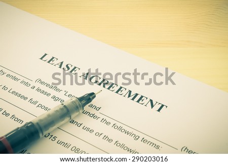 Lease agreement contract sheet and brown pen at bottom left corner on wood table background in vintage style