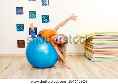 Laughing girl from a primary school lying on a large blue gymnastic ball