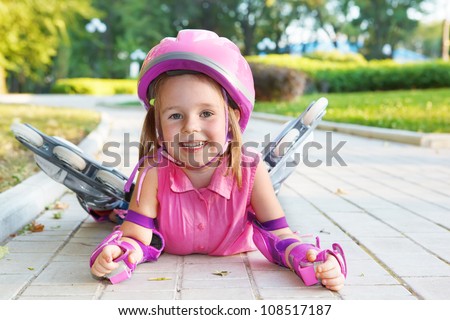 Cheerful preschool girl wearing inline roller skates and protective equipment
