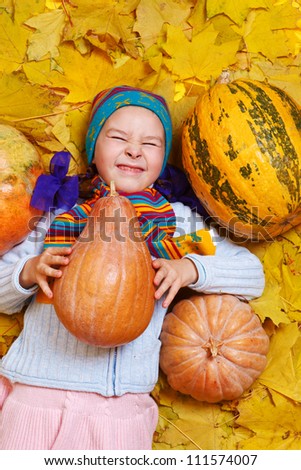 Sweet smiling little girl in knitwear, lying with pumpkins