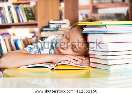 Tired primary school student sleeping in a library