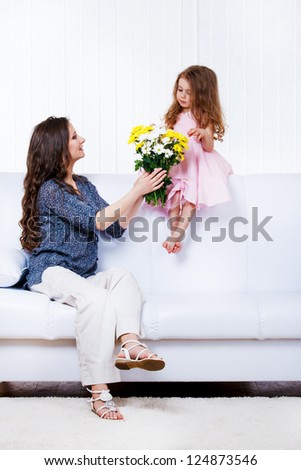 Mother with  flowers bouquet and little daughter sitting on sofa
