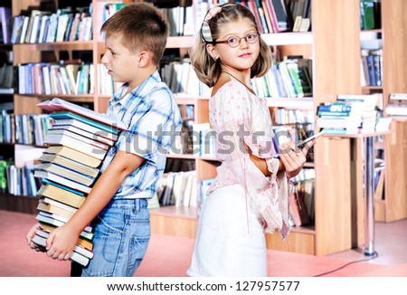 Boy holding pile of paper books and girl with an electronic book