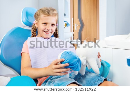 School aged girl in a dental chair holding toy teeth in hands
