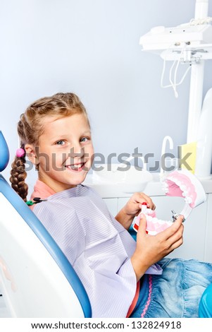 Smiling school aged girl cleaning toy dentures with a toothbrush