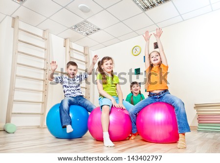Cheerful kids on large gym balls with their hands up