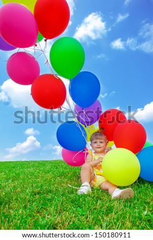 Sweet toddler girl sitting on green grass with a bunch of balloons