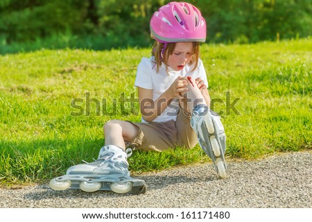 Preschool roller skate beginner looking at her bleeding knee.