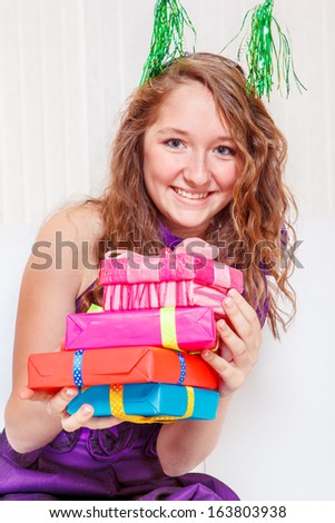 Cute cheerful teenage girl in a party dress with a pile of gift boxes
