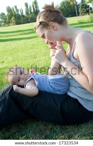 Mother sitting on the lawn and kissing or biting baby toes