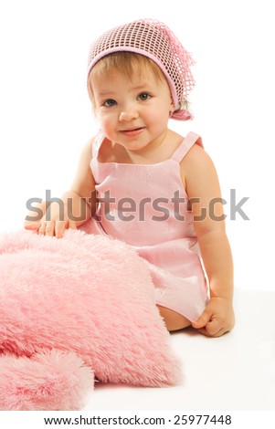 Sweet toddler in pink sitting beside fluffy pillows