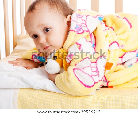 Baby in bathrobe lying in crib with puppy toy