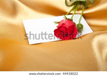 Red rose and blank invitation card on golden satin