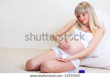 A beautiful pregnant woman sitting on the floor and applying cream