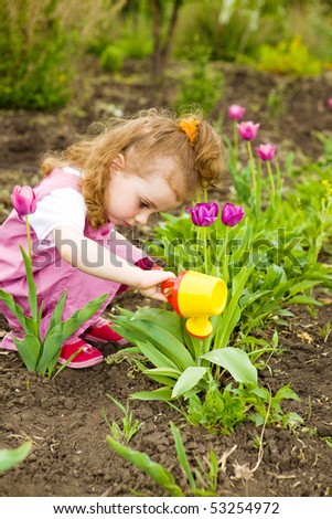 Cute curly girl watering flowers in the garden