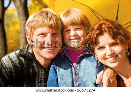 Happy family of three under umbrella in the autumn park