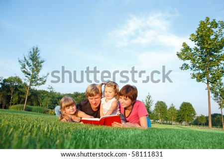Sweet family reading a book on the green grass