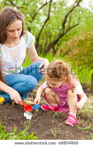 Curly toddler daughter helping her mom in the garden