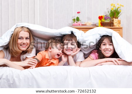 Laughing woman and kids covered with blanket