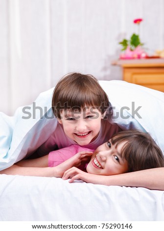 Happy brother and sister covered with blanket