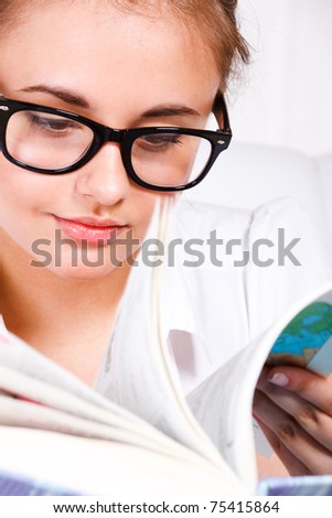 Portrait of a teenage girl in glasses turning book pages